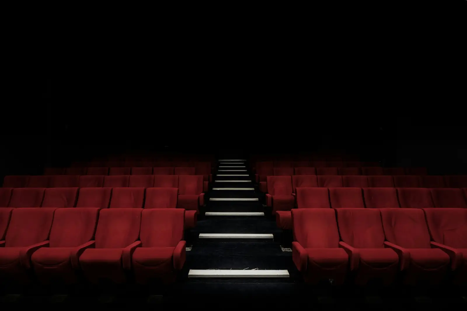 Karanlık sinema salonunda kırmızı koltuk sıraları ve ortadaki merdiven