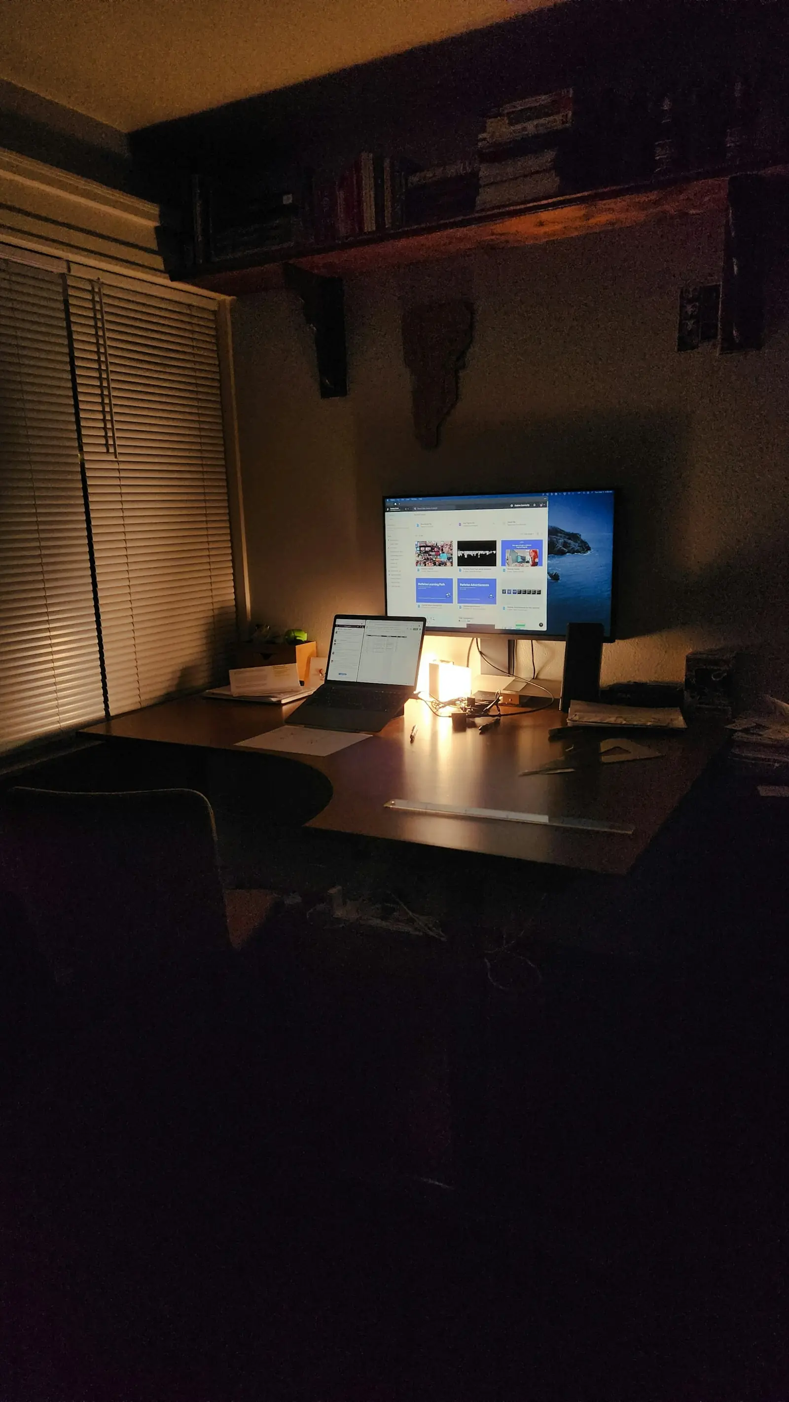 Gece masa lambasıyla aydınlanan, monitör ve dizüstü bilgisayarlı ev ofisi
