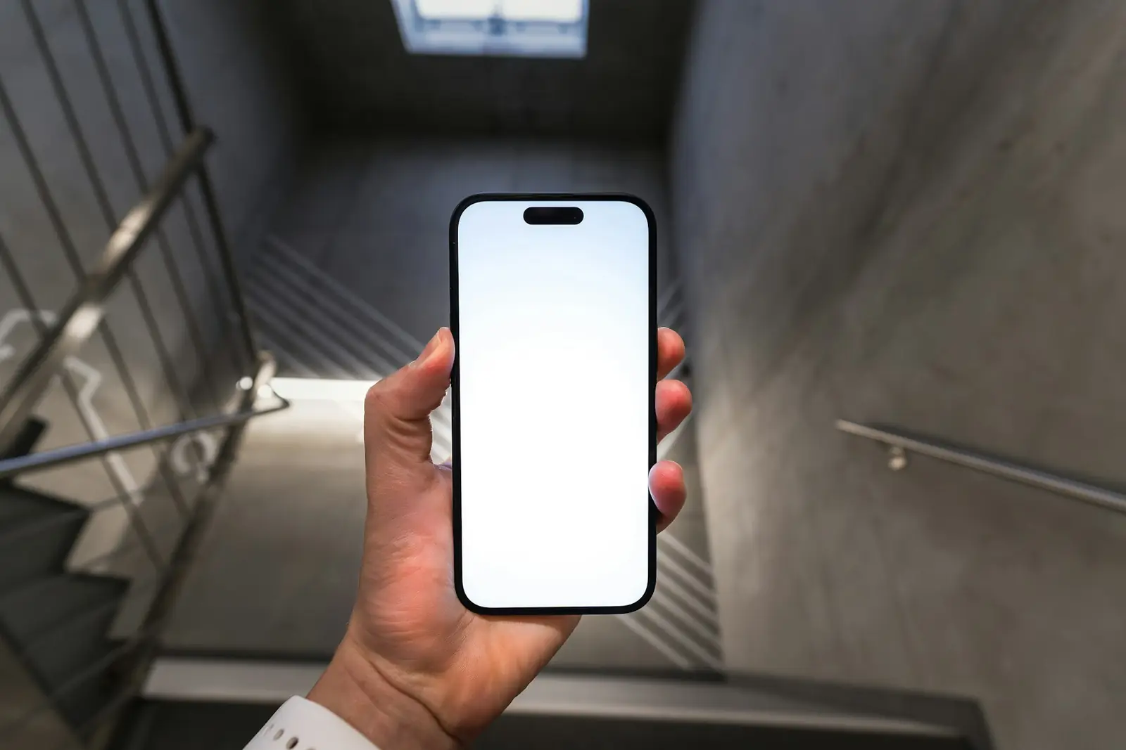 Beton merdiven boşluğunda boş beyaz ekranlı akıllı telefonu tutan el