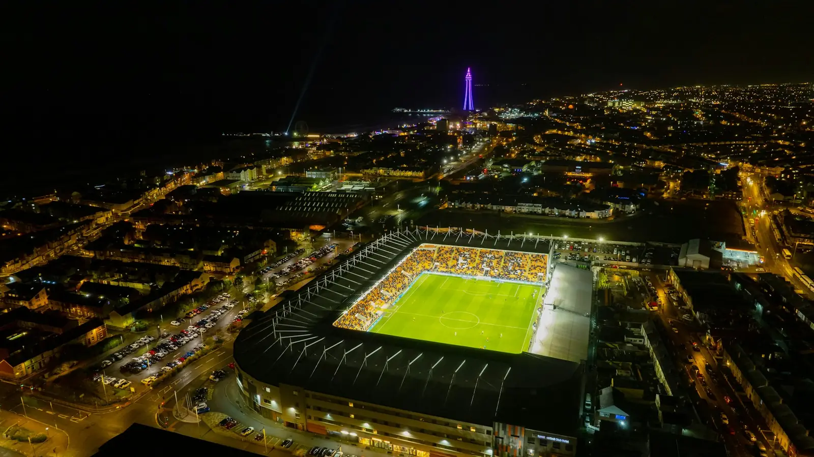 Gece şehir ışıkları arasında aydınlatılmış futbol stadyumunun havadan görünümü