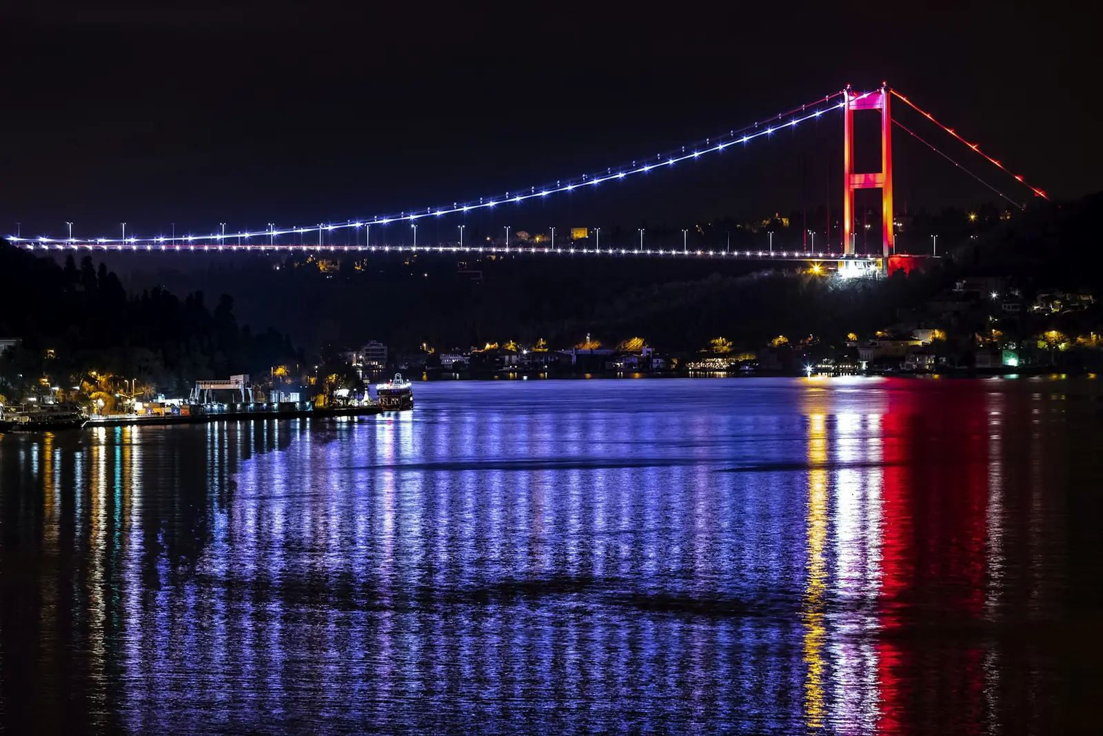 Gece mor ve kırmızı ışıklarla aydınlatılmış İstanbul Boğazı köprüsü ve sudaki yansımaları